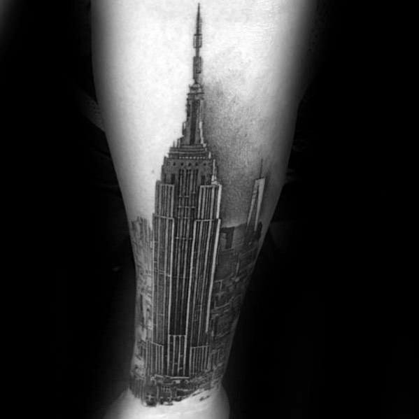 Empire State Building tattoo with intricate skyline details and dramatic black shading, positioned on a man's forearm.