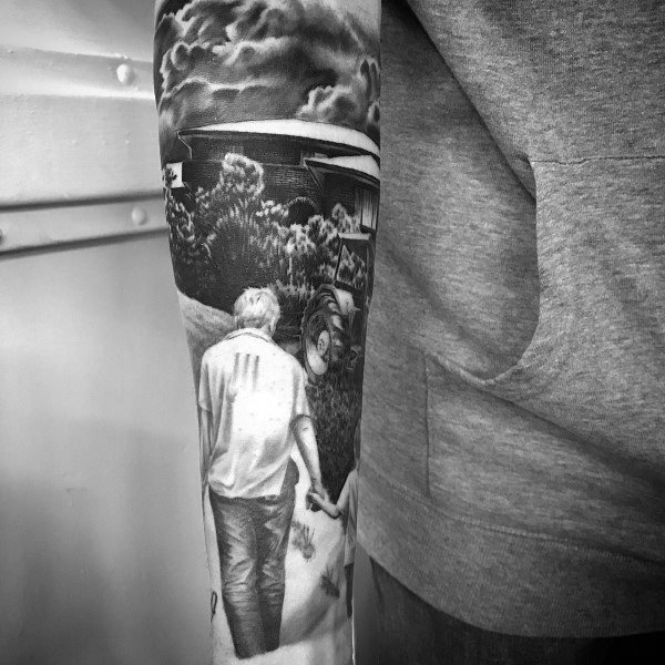 Realistic black and gray farming tattoo of a man holding a child’s hand, walking towards a tractor and barn under a cloudy sky.