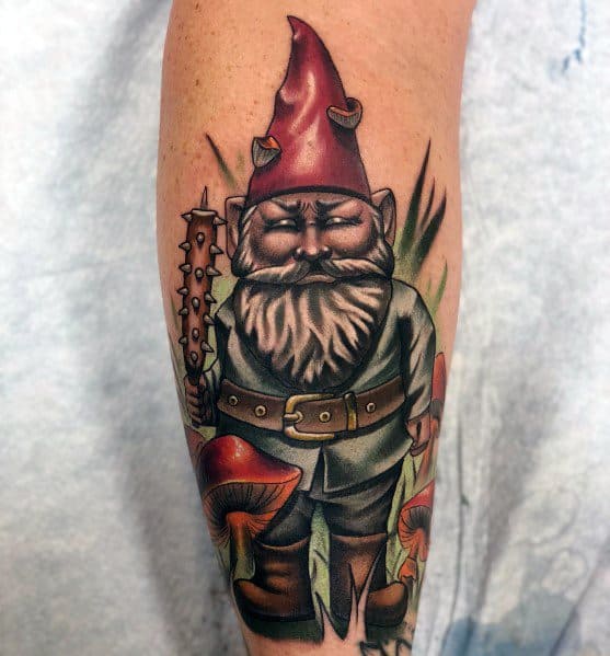 Tattoo of a fierce gnome with a spiked red hat, white beard, and gray outfit, holding a spiked club, surrounded by mushrooms and greenery.