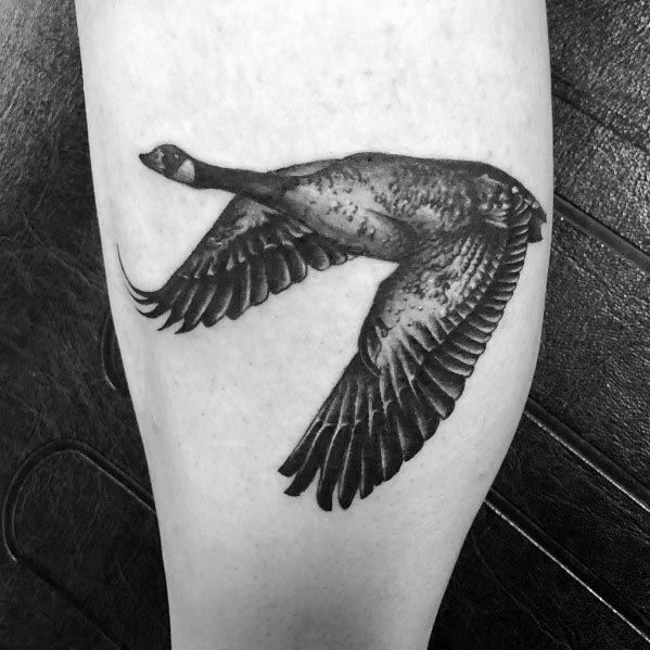 Realistic black and gray tattoo of a flying goose, inked with detailed shading and fine linework, placed on the forearm or calf.