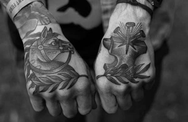 Matching hand tattoos in blackwork style featuring a horse head with laurel on one hand and an anvil with nails and radiant lines on the other.