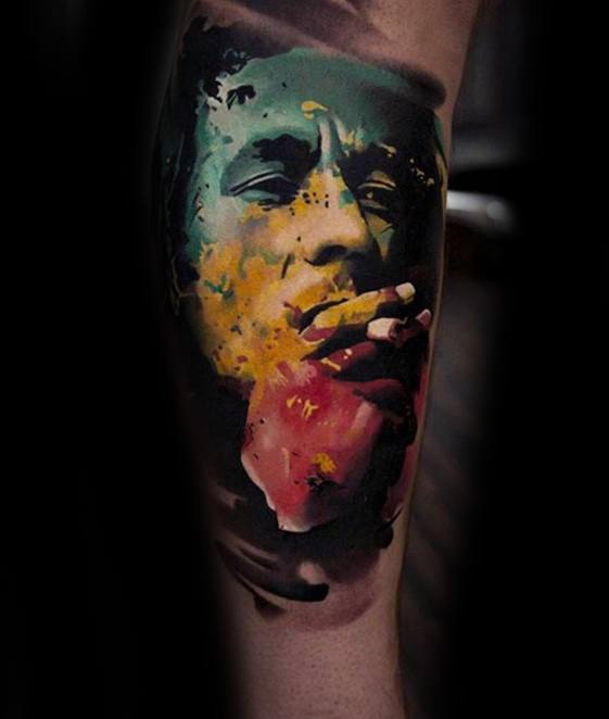 Vibrant Bob Marley tattoo with bold splashes of yellow, green, and red, showing him smoking in a modern watercolor realism style.