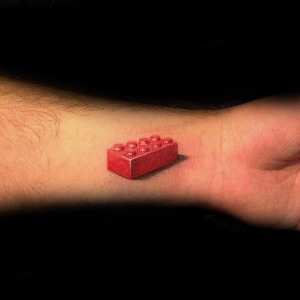 Hyper-realistic tattoo of a red Lego brick on the inner wrist, featuring sharp shadows and 3D effect for a lifelike appearance.