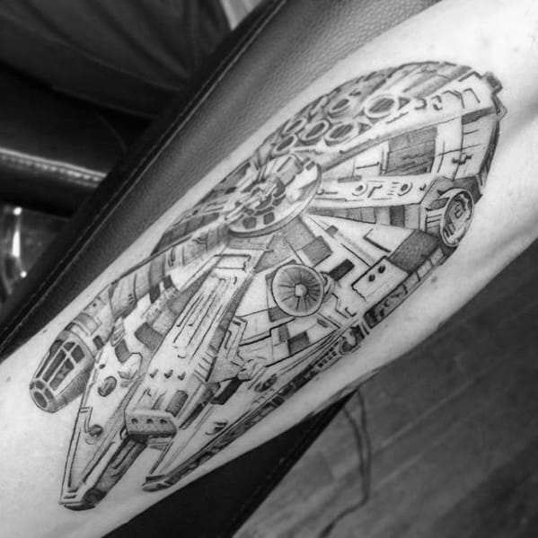 Detailed black and grey Millennium Falcon tattoo on the forearm, showcasing intricate shading and mechanical texture.