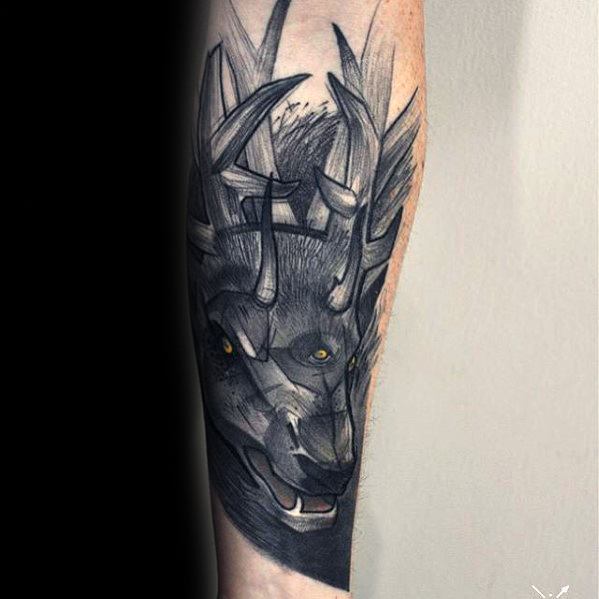 Stylized Witcher tattoo of the Leshen creature with antlers and glowing eyes, inked in black and grey on the forearm.