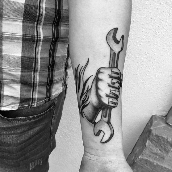 Black and grey tattoo of a hand gripping a wrench with the word UNITY across the fingers, symbolizing strength and solidarity.