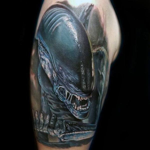 Hyper-realistic Xenomorph tattoo on upper arm showing the creature snarling with glistening black skin and extended clawed hand.