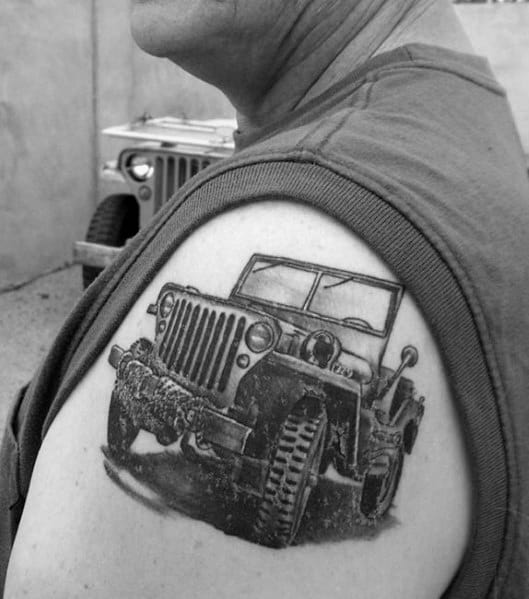 Realistic black and grey tattoo of a classic Jeep on the upper arm, showcasing rugged details and an off-road stance.