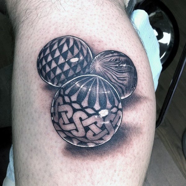 Black and gray tattoo of three marbles with intricate geometric, woodgrain, and Celtic knot patterns, creating a bold 3D effect on the skin.