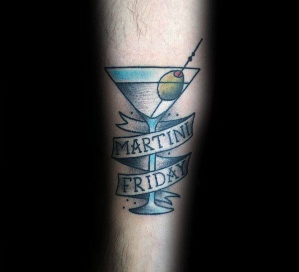 Traditional-style martini glass tattoo with an olive garnish and a banner reading "Martini Friday." A classic and fun design with bold lines.
