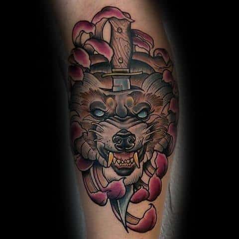 Neo-traditional tattoo of a snarling wolf with a dagger piercing through its head, surrounded by bold pink petals and intricate shading.