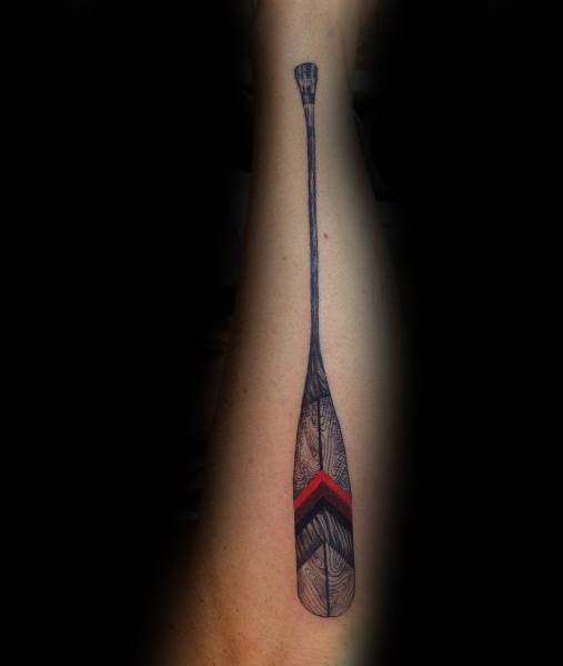 Realistic paddle tattoo on the forearm with intricate wood grain details and a bold red and black geometric design, symbolizing adventure and strength.