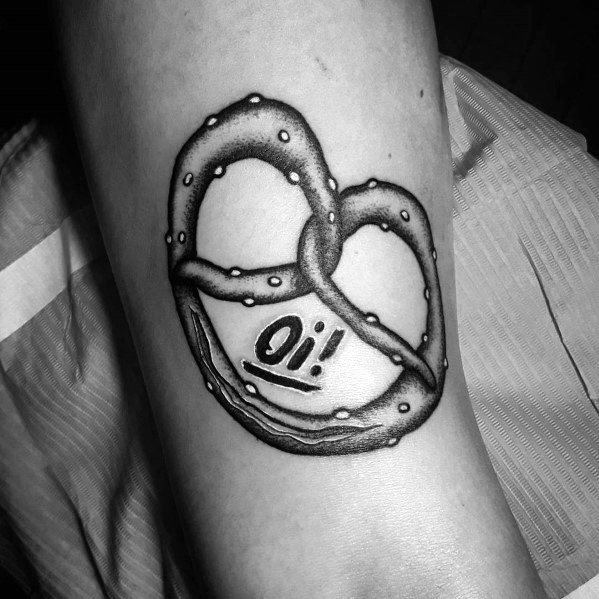 Black and grey pretzel tattoo with realistic shading, salt details, and the word "Oi!" written below in bold lettering.