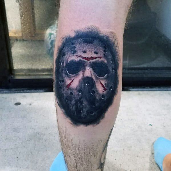 Realistic tattoo of Jason Voorhees' hockey mask from *Friday the 13th*, featuring dark shading, blood splatters, and a hauntingly detailed design.