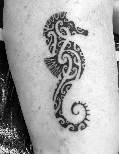 Tribal-style seahorse tattoo on upper arm, featuring bold black ink with intricate swirling patterns for a striking and symbolic design.