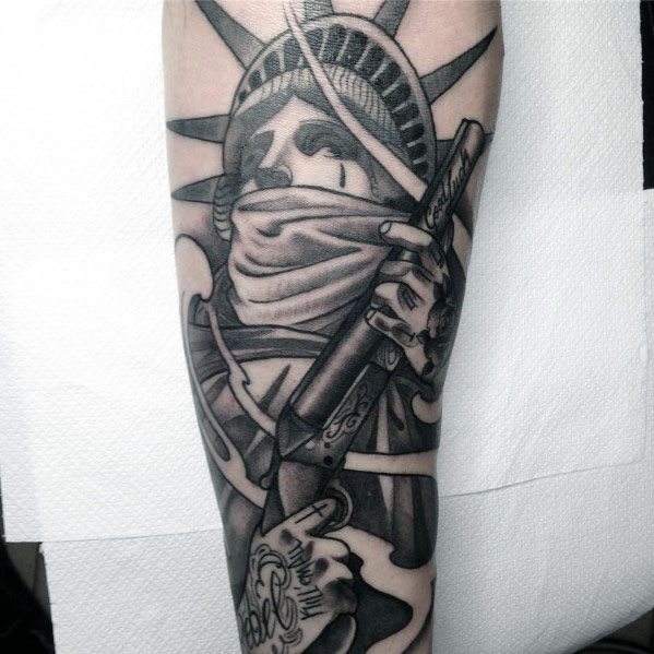 Black and grey tattoo of the Statue of Liberty wearing a bandana and holding a shotgun, featuring bold shading and intricate details.
