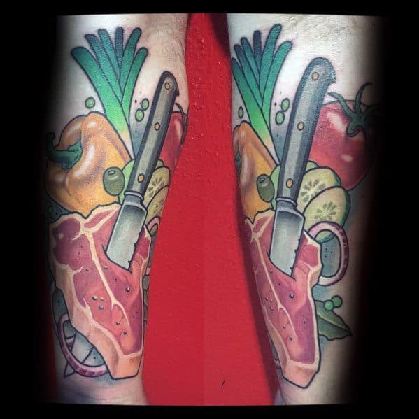 Tattoo of a steak with a knife stabbed into it, surrounded by colorful vegetables like peppers, tomatoes, and greens for a bold food-themed design