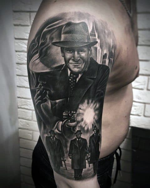 Black and grey gangster tattoo featuring a suited mobster firing a Tommy gun, with dramatic shading and a vintage crime scene aesthetic.