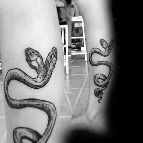 Minimalist black and grey two-headed snake tattoo slithering along the leg, featuring fine line details for a sleek and elegant look.