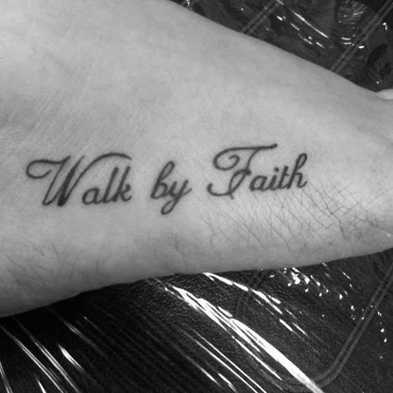 Ankle tattoo with "Walk by Faith" in a delicate cursive script, creating a simple yet meaningful design symbolizing trust and belief.