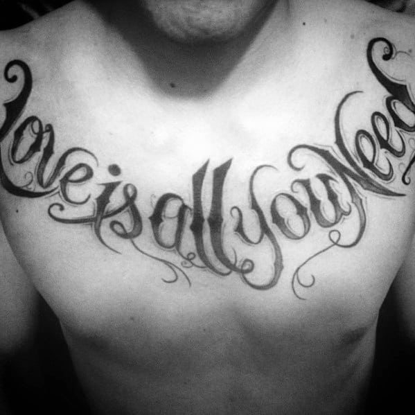 Chest tattoo featuring the iconic Beatles lyric "Love is all you need" in bold, flowing script that stretches across the collarbone.