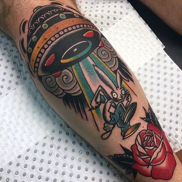 Tattoo of a cartoon-style UFO beaming up a rabbit, with bold lines and bright colors, accompanied by a red rose, creating a playful and surreal design.