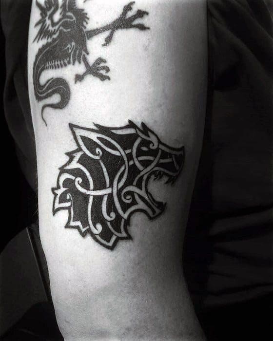 Celtic wolf head tattoo on upper arm with bold black lines and tribal knotwork forming a fierce, angular silhouette.