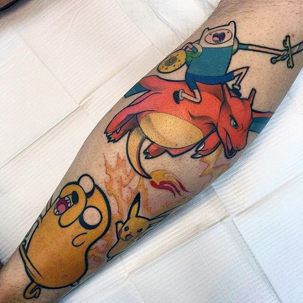 Fun crossover tattoo featuring Charizard ridden by Finn with Jake and Pikachu nearby, in bold cartoon-style color on the forearm.