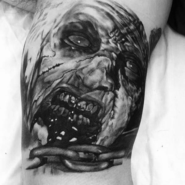 Realistic black and grey Evil Dead tattoo of a decaying, chained deadite face with rotting teeth, torn skin, and a haunting expression.