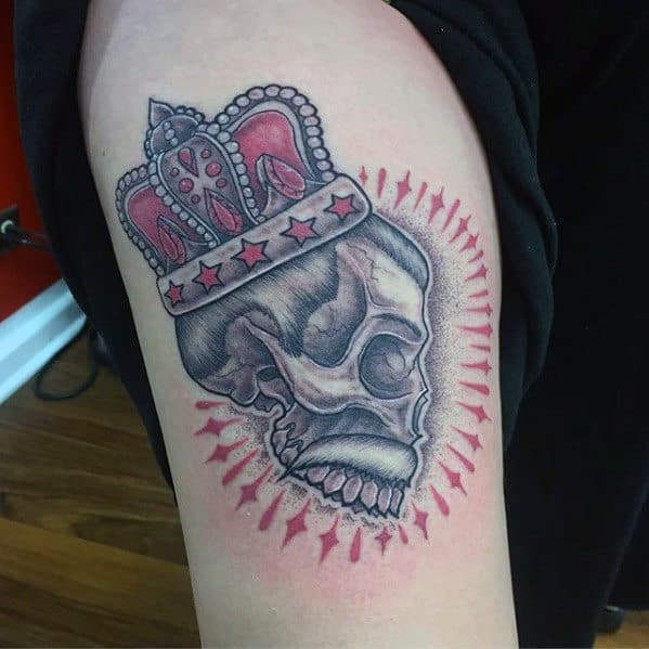 Tattoo of a skull wearing a jeweled crown, surrounded by red rays, symbolizing Freddie Mercury’s title as the rock 'n' roll royalty.