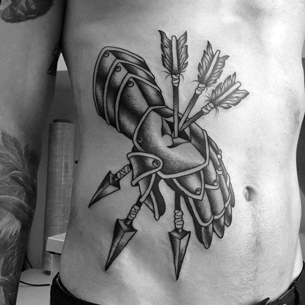 Black and grey tattoo of an armored gauntlet pierced by three large arrows, placed across the ribs with bold shading and sharp detail.