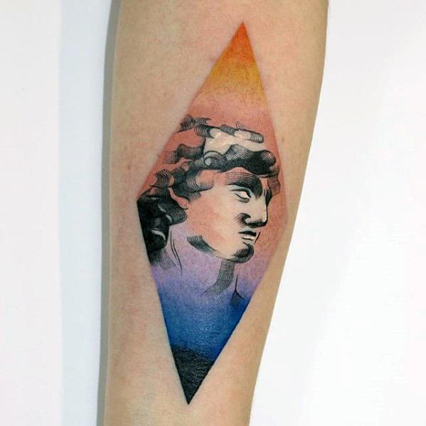 Tattoo of a classical sculpture head inside a diamond shape with a smooth gradient background transitioning from orange to purple to blue.