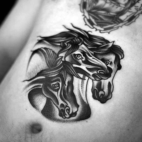 Stylized black and grey tattoo of three horse heads with bold lines and shading, placed on the side of the torso