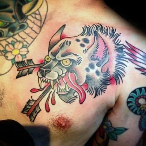 Traditional-style hyena head tattoo on the chest with bold lines, vivid colors, and arrows piercing through, dripping with stylized blood.