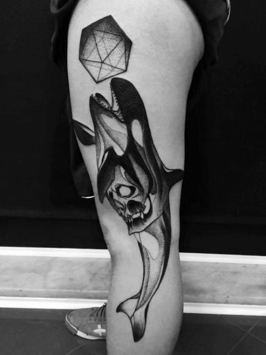 Tattoo of an orca with a skull embedded in its body, paired with an icosahedron above the thigh in a bold black and gray style.