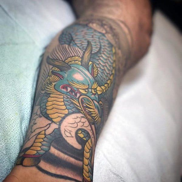 Colorful Kirin tattoo on the calf with teal, gold, and pink tones, featuring flowing mane and bold scales in a traditional Japanese style.