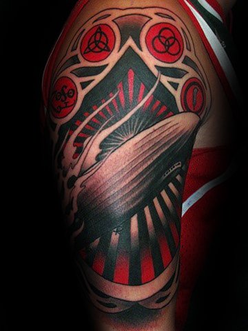 Bold red and black upper arm tattoo of a Zeppelin airship with radiant beams and all four Led Zeppelin symbols in circular frames above.