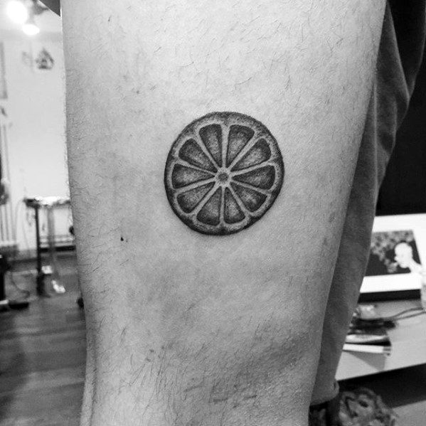 Small black and grey tattoo of a lemon slice viewed from above, with clean segments and subtle shading for a 3D effect.