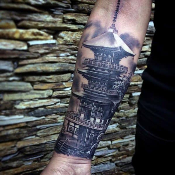 Detailed forearm tattoo of a Japanese pagoda in black and grey with realistic shading and cloudy sky background.