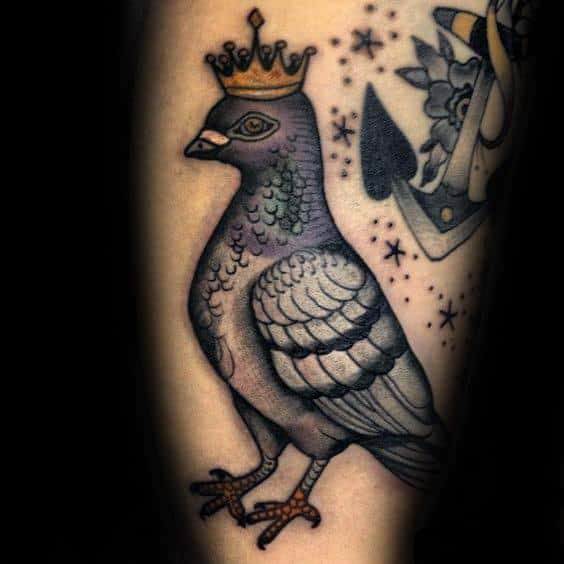 Traditional-style pigeon tattoo wearing a gold crown, surrounded by stars, symbolizing pride, royalty, and uniqueness.