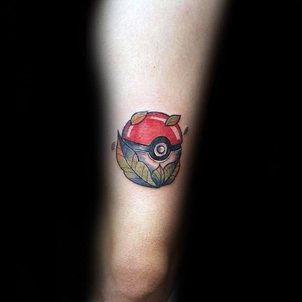 Minimalist Pokeball tattoo wrapped in soft green leaves, blending nature and Pokémon in a clean, subtle forearm design.