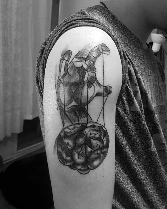 Black and grey puppet tattoo of a hand controlling a human brain with strings, symbolizing manipulation or control of thoughts.