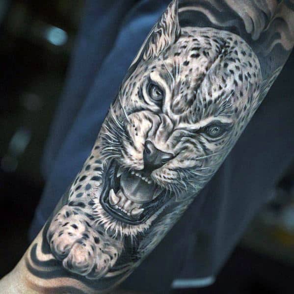 Hyper-realistic snow leopard tattoo in black and gray on the forearm, showing the fierce feline mid-snarl with intense detail.