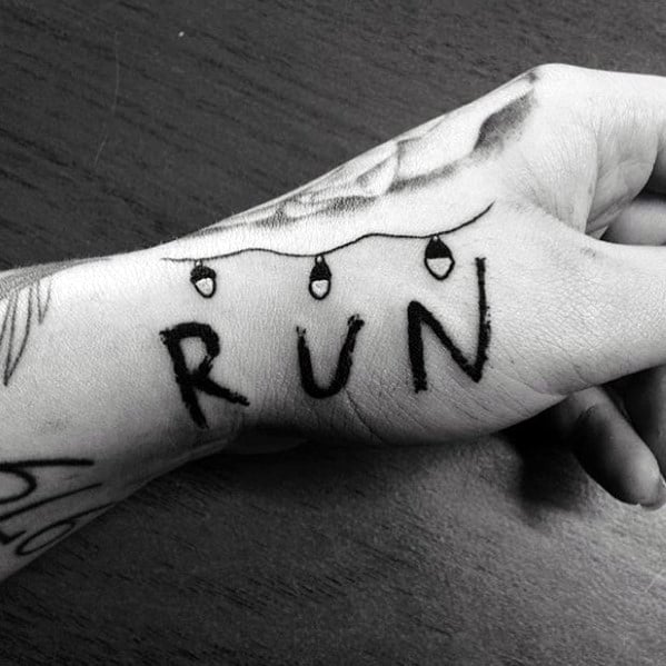 Simple black tattoo of the word “RUN” on the hand, with Christmas lights above, inspired by Stranger Things' eerie wall message scene.