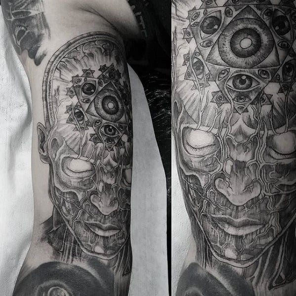 Black and grey Tool-inspired tattoo of a surreal face with blank eyes, geometric patterns, and multiple all-seeing eyes on the forehead.