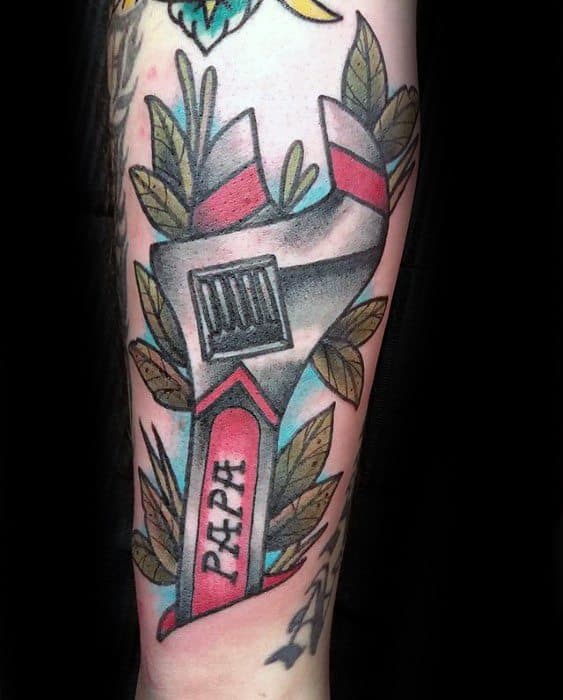 Colorful tattoo of an adjustable wrench with red accents, surrounded by green leaves and the word PAPA written down the handle.
