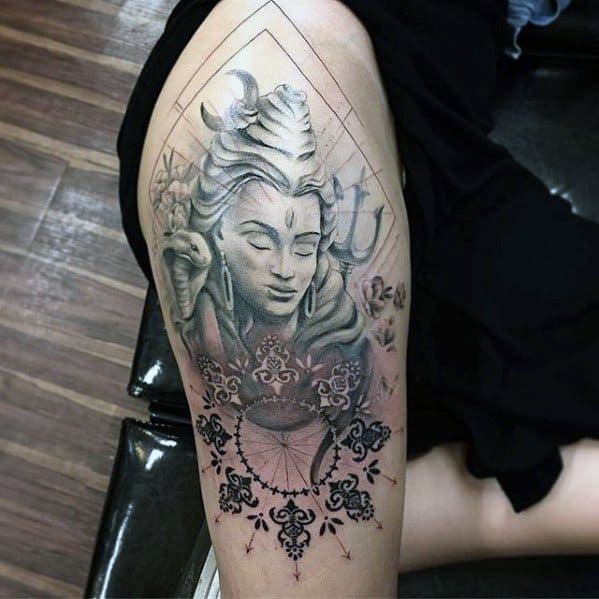 Thigh tattoo of Lord Shiva with a peaceful expression, crescent moon, snake, trishul, and ornamental mandala blending into delicate floral patterns.