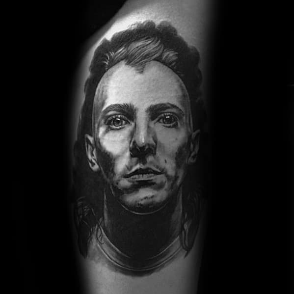 Realistic black and grey portrait tattoo of a man with intense expression and detailed shading, placed on the upper arm.