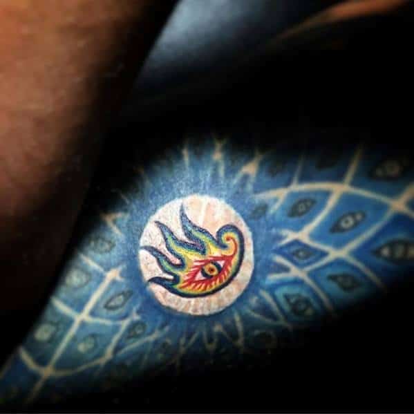 Colorful Tool-inspired tattoo featuring the iconic flaming eye logo within a circular frame, surrounded by a vivid blue pattern of watching eyes.