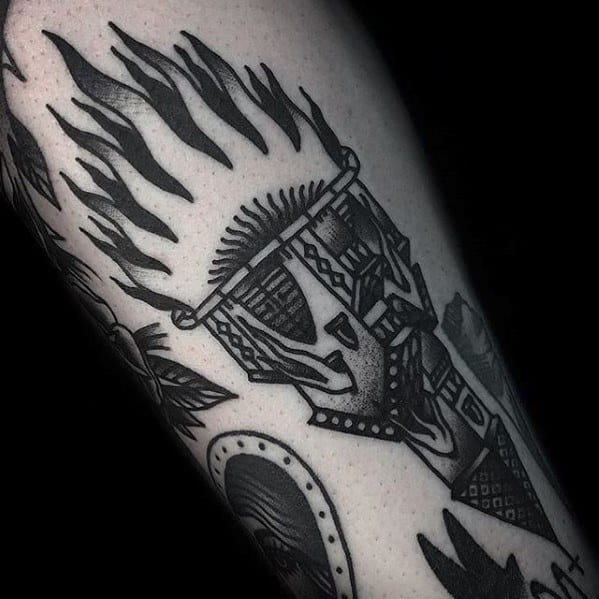 Bold blackwork torch tattoo featuring a tribal mask design, sharp flames, and heavy geometric shading for a striking effect.